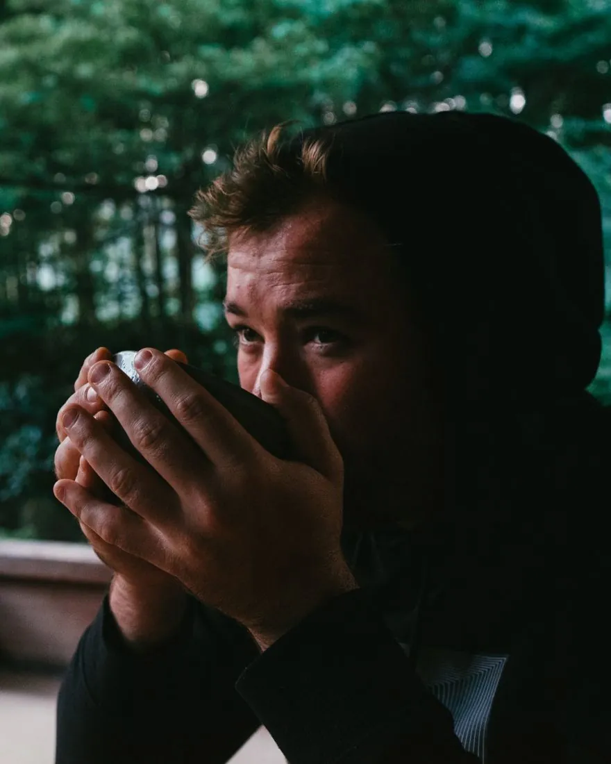 Maans Dye, une tasse de thé à la main, sous une véranda en bois devant un jardin